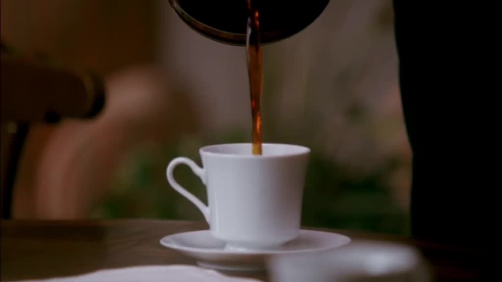 She picks up the coffee pot, and starts pouring coffee into a mug.jpg