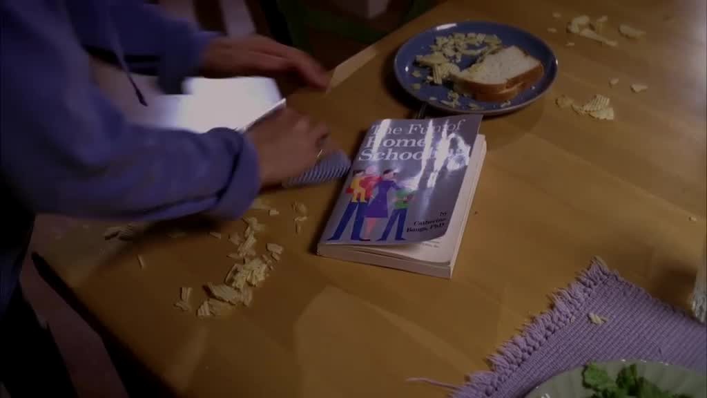 Lynette is clearing up crumbs from the table, the book is open on the table.jpg