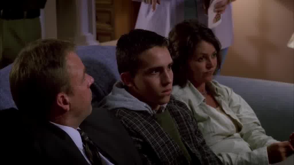 the shot pans down to see a teenage boys quashed in between his parents on a sofa.jpg
